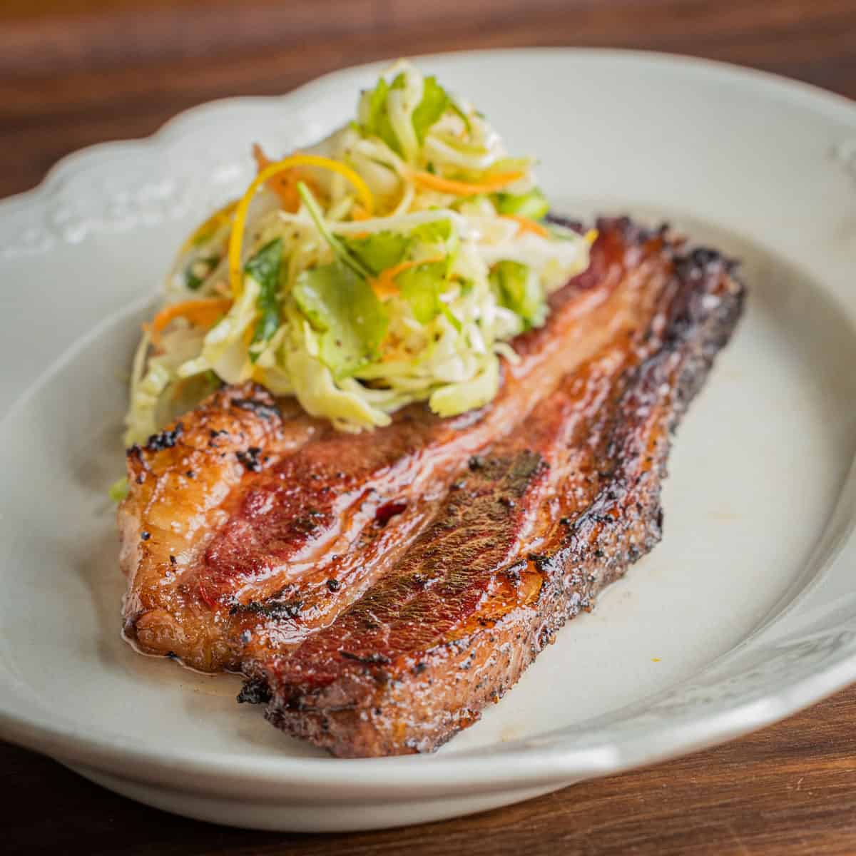 A cooked bacon steak on a plate with coleslaw.