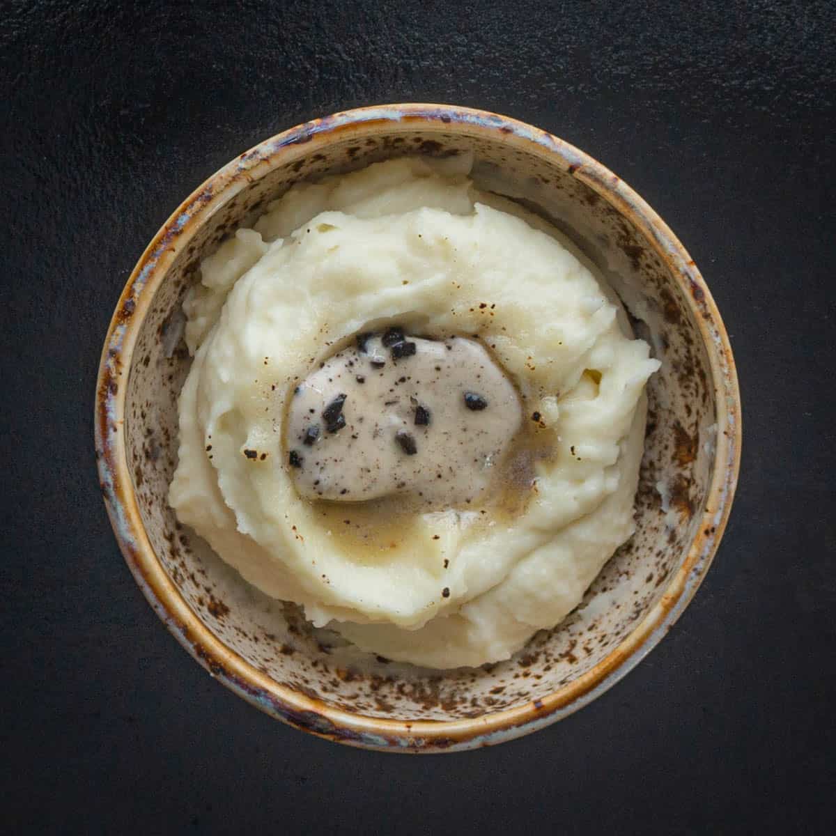 mashed potatoes in a ceramic bowl with a slice of truffle butter melting on top.