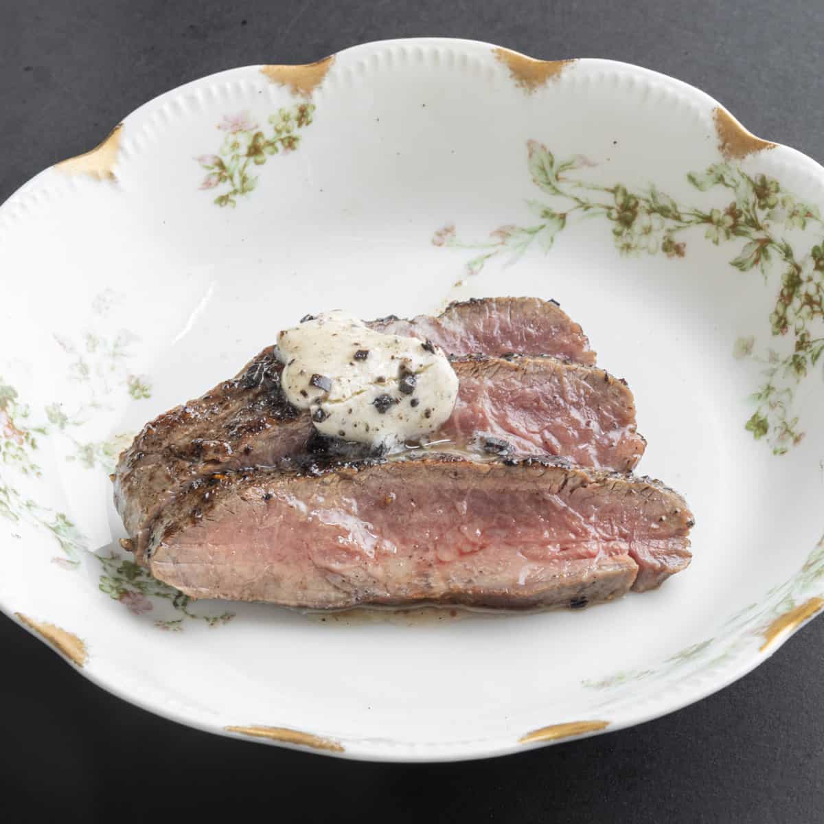 A sliced steak on a china plate with truffle butter melting over the top.