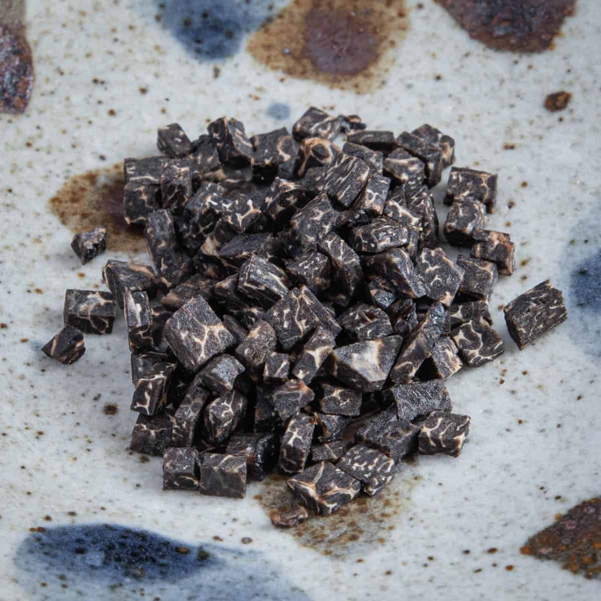 Finely chopped black truffle next to a sliced truffle and a knife.