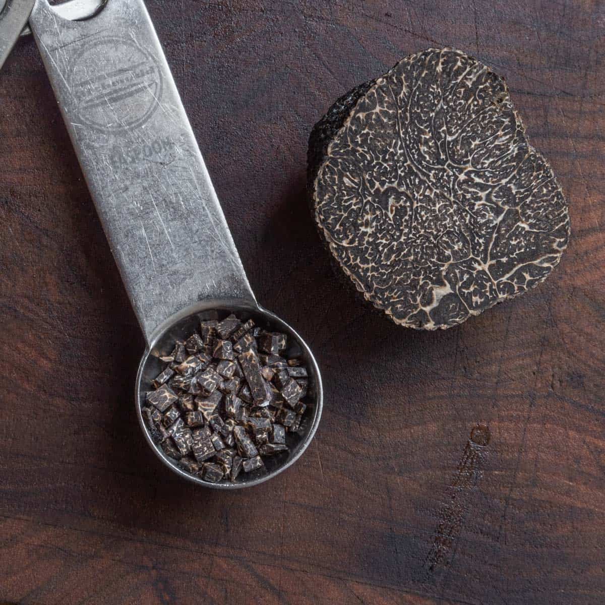 chopped truffle in a metal teaspoon next to a cut black truffle.