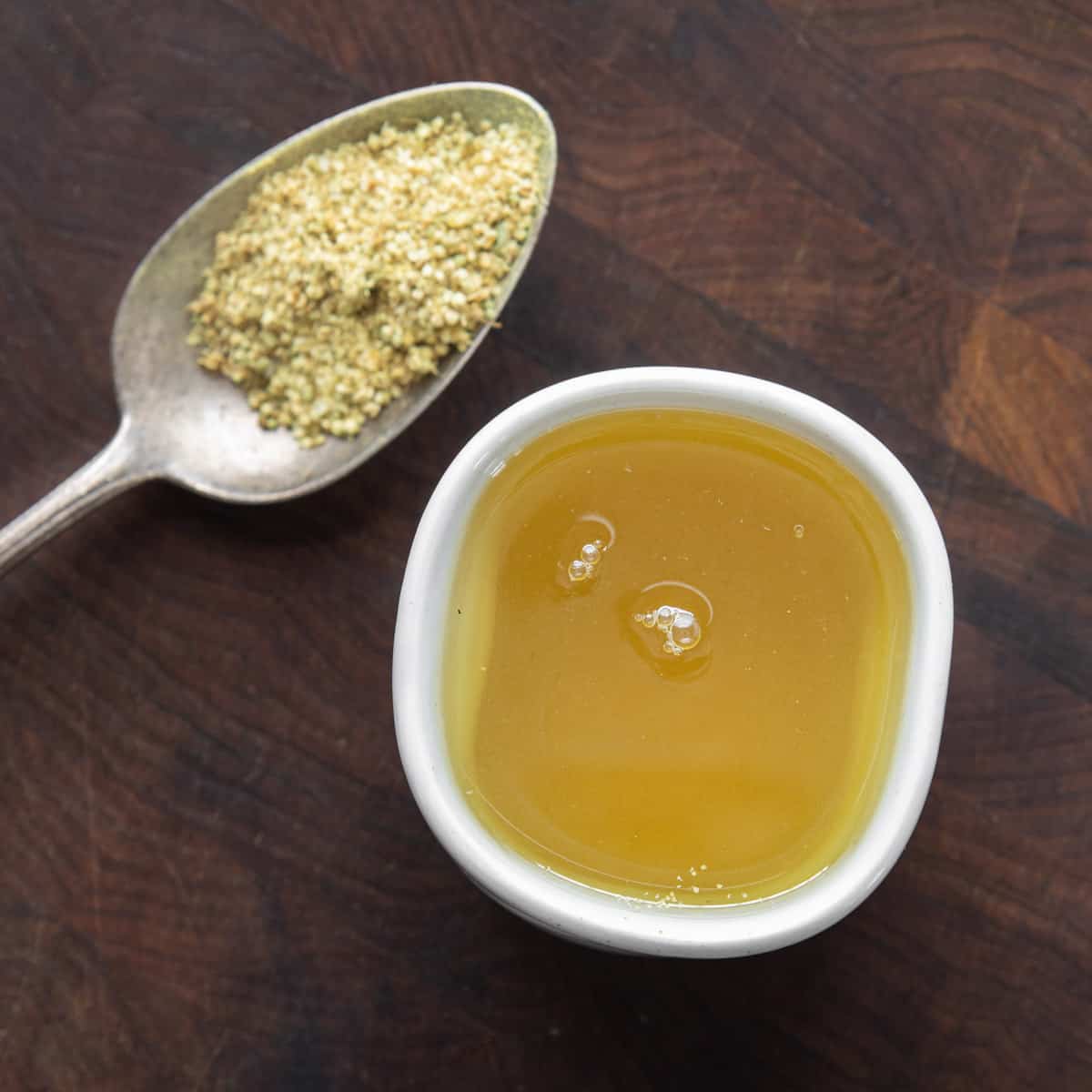 Meadowsweet tea in a cup next to a spoonful of meadowsweet flowers 