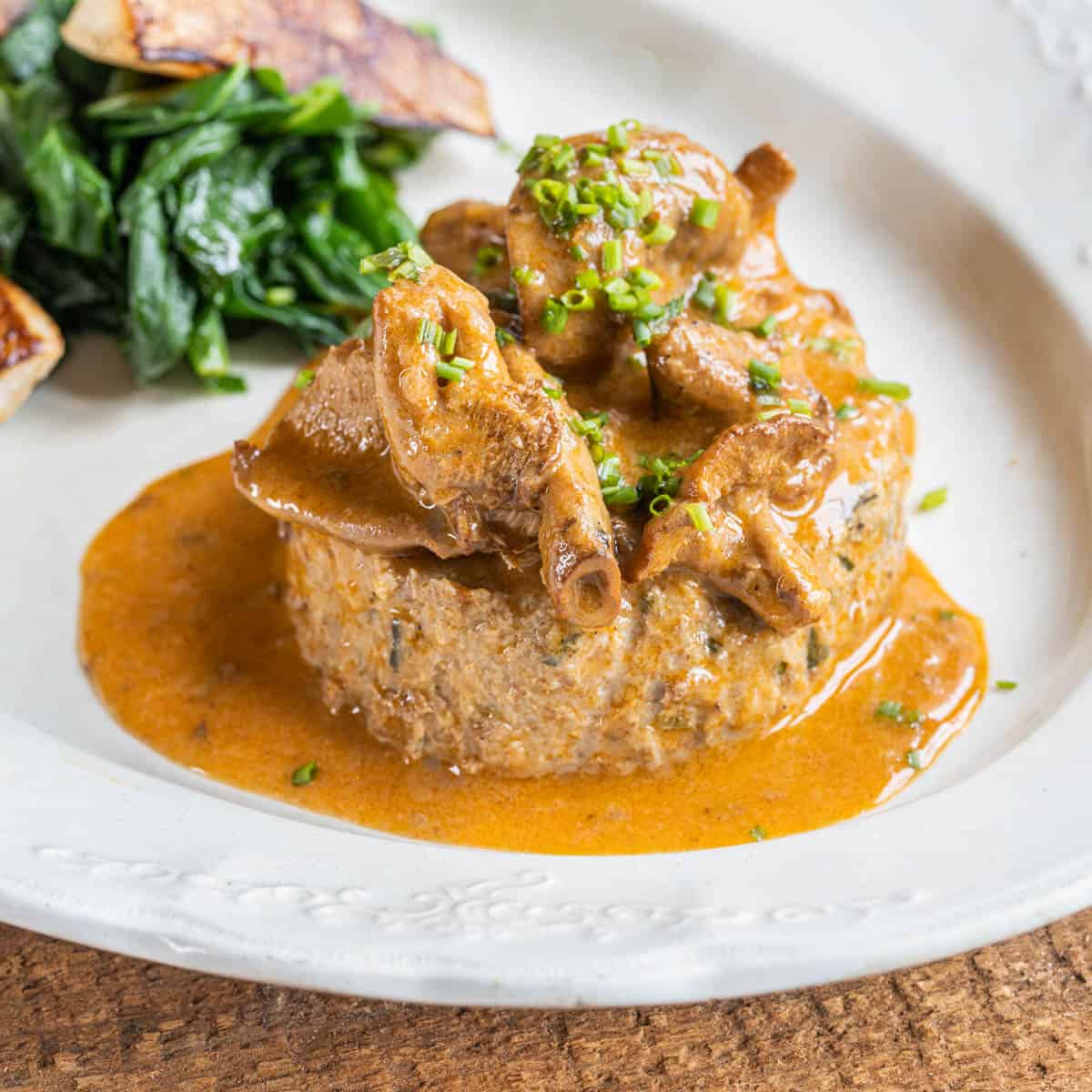 A slice of meatloaf on a plate with hedgehog mushrooms in sauce. 