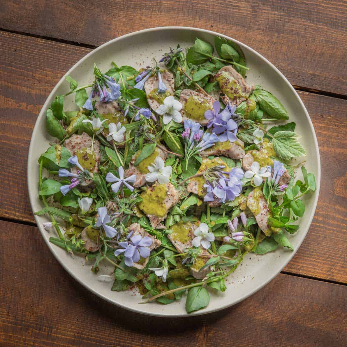 A salad of watercress and spring vegetables with cooked tongue and purple and white wild flowers.