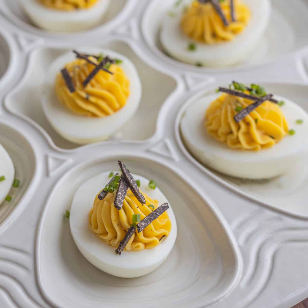 Black truffle deviled eggs on a plate garnished with sliced truffles and chives. 