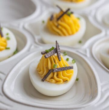 Black truffle deviled eggs on a plate garnished with sliced truffles and chives.