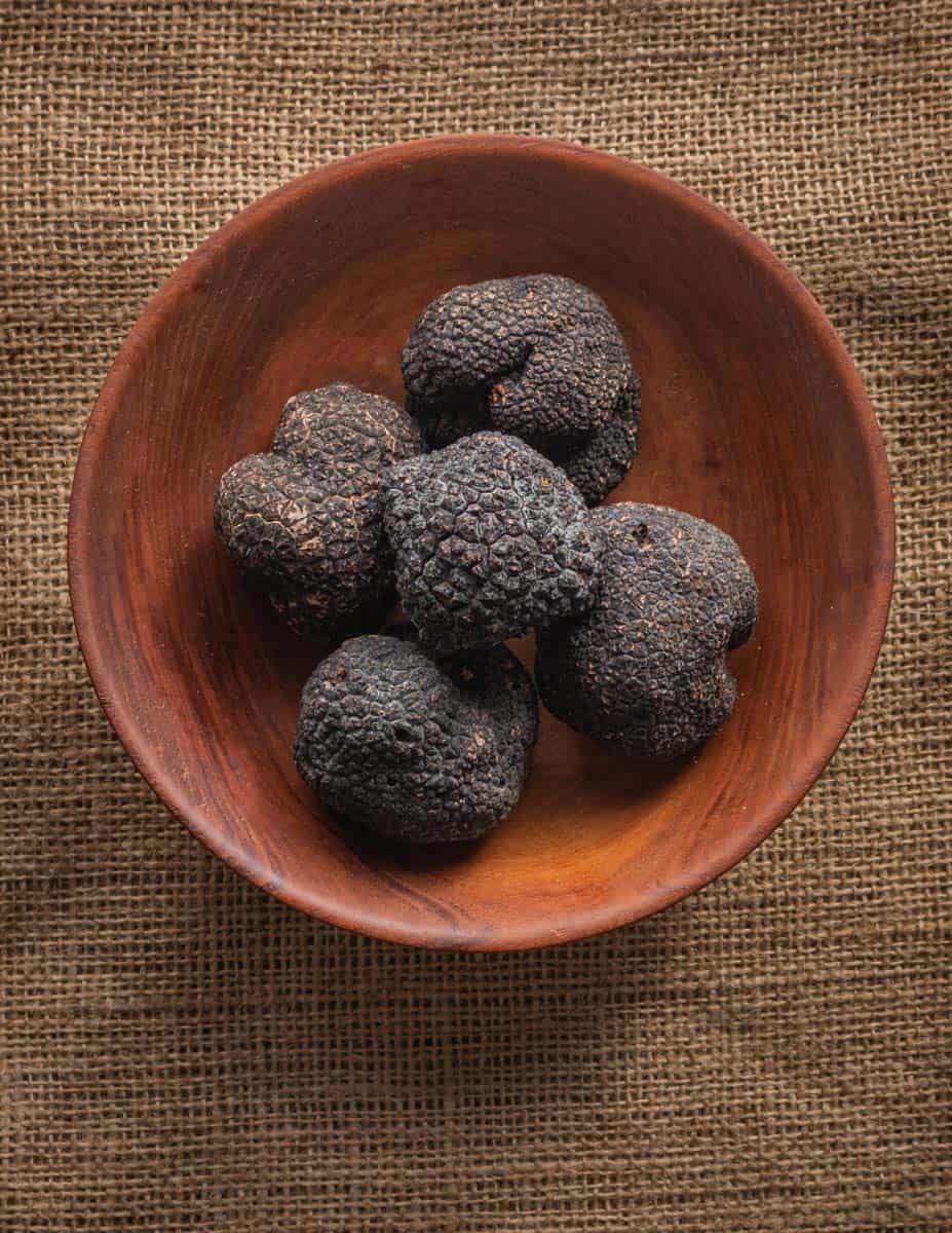 A bowl filled with 5 fresh, black Italian truffles on a burlap background.