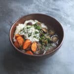 Lamb neck stew in a ceramic bowl on a slate background.