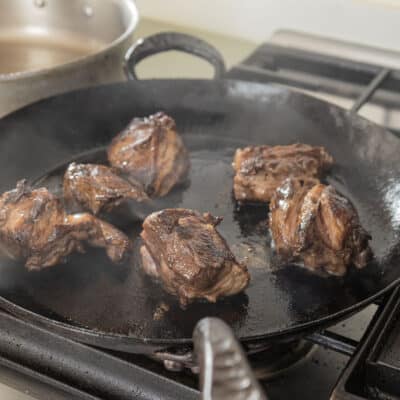 Browning pieces of lamb neck in a carbon steel pan. 