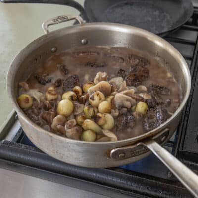 Adding mushrooms and onions to a pot of lamb neck stew. 