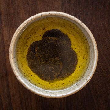 A ceramic bowl of oil with sliced black truffles on the bottom.