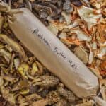 a log of mushroom butter on a board surrounded by different types of dried mushrooms.