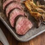 A cooked, sliced, juicy pink steak on a tray next to roasted oyster mushrooms.