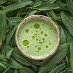 A top down image of a ceramic bowl filled with green soup surrounded by wild garlic leaves.