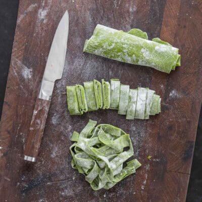 Rolled up green ramp pasta being cut into noodles with a knife. 