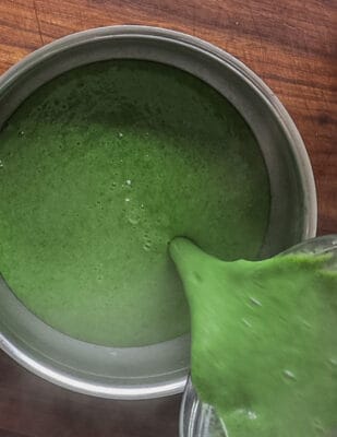 Pouring stinging nettle soup from a blender into a metal mixing bowl.