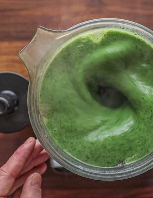 A top down image of a blender with the lid off pureeing stinging nettle soup.