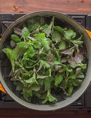 A top down image of cooking nettles in a pot with a steamer.