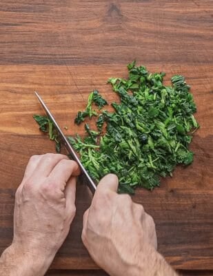 Chopping cooked stinging nettles with a chefs knife.
