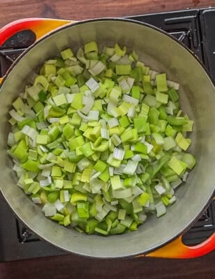 A top down image of cooking leeks, celery and onion in butter in a soup pot.