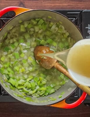 A top down image of pouring chicken stock onto cooked celery, onion and leeks.