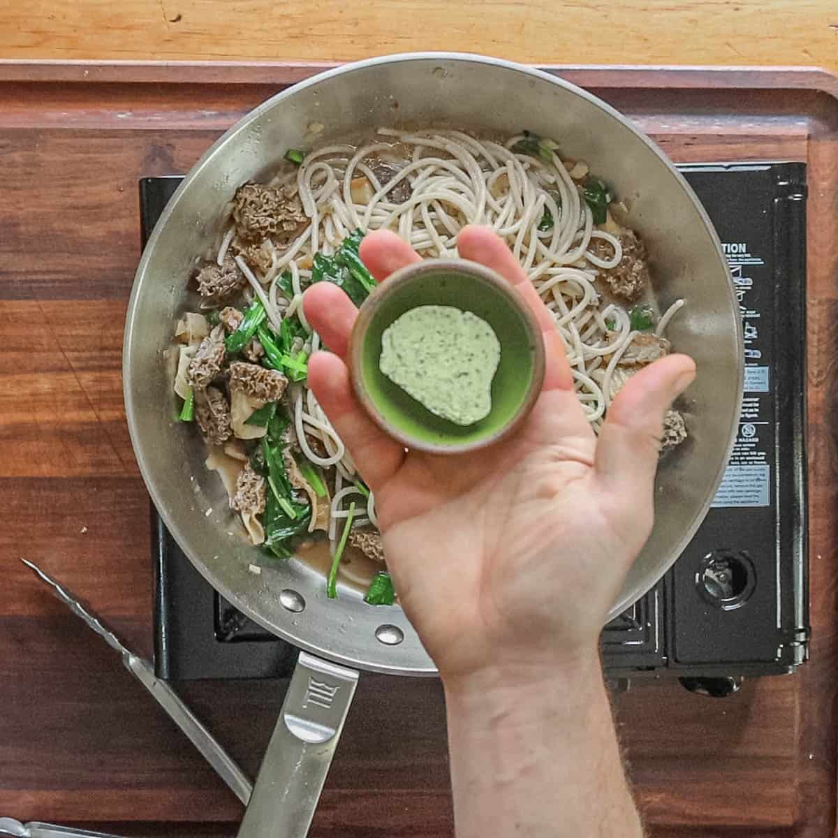 Adding ramp butter to the pan of ramps and morel pasta. 