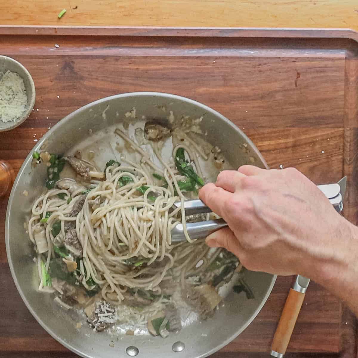 Twirling pasta with tongs before plating. 