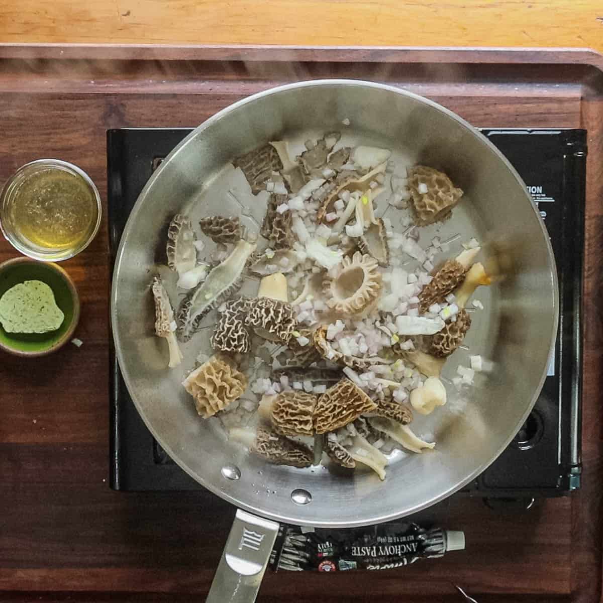 Adding shallot and garlic to a pan of morel mushrooms. 