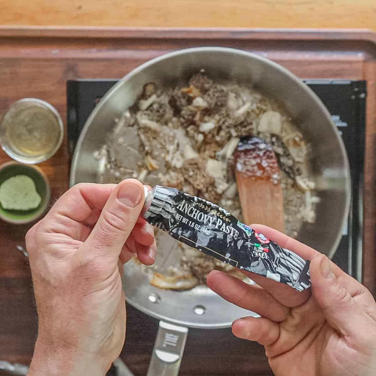 Adding anchovy paste to a pan of morel mushrooms. 