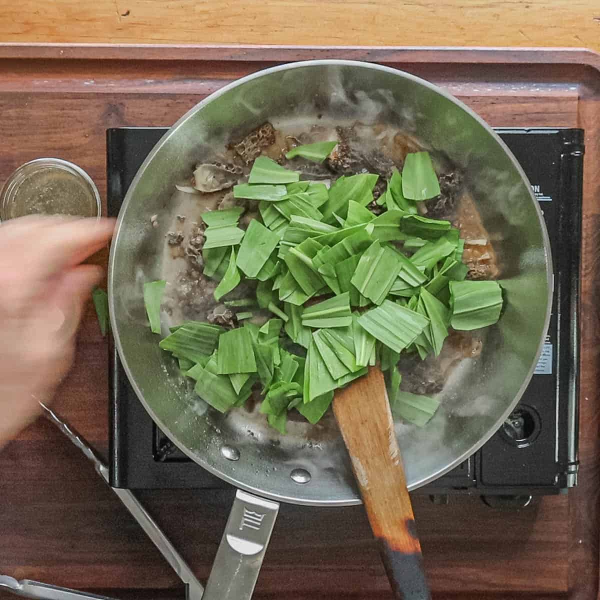 Adding ramp leaves to a pan of morel mushrooms. 