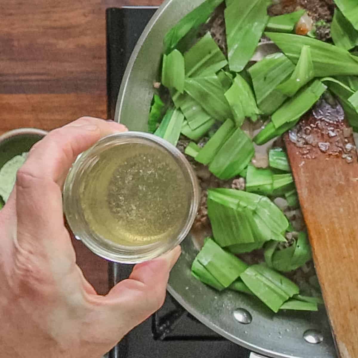 Adding chicken stock to a pan of ramp and morel pasta sauce. 