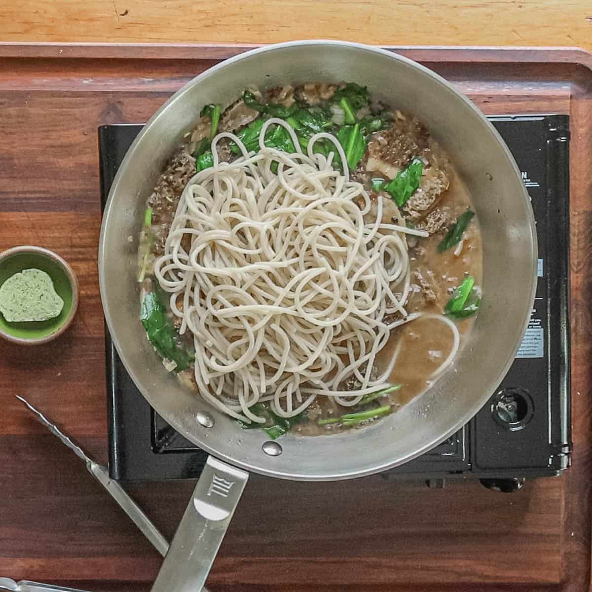 Adding pasta to a pan of cooked ramps and morel mushrooms. 