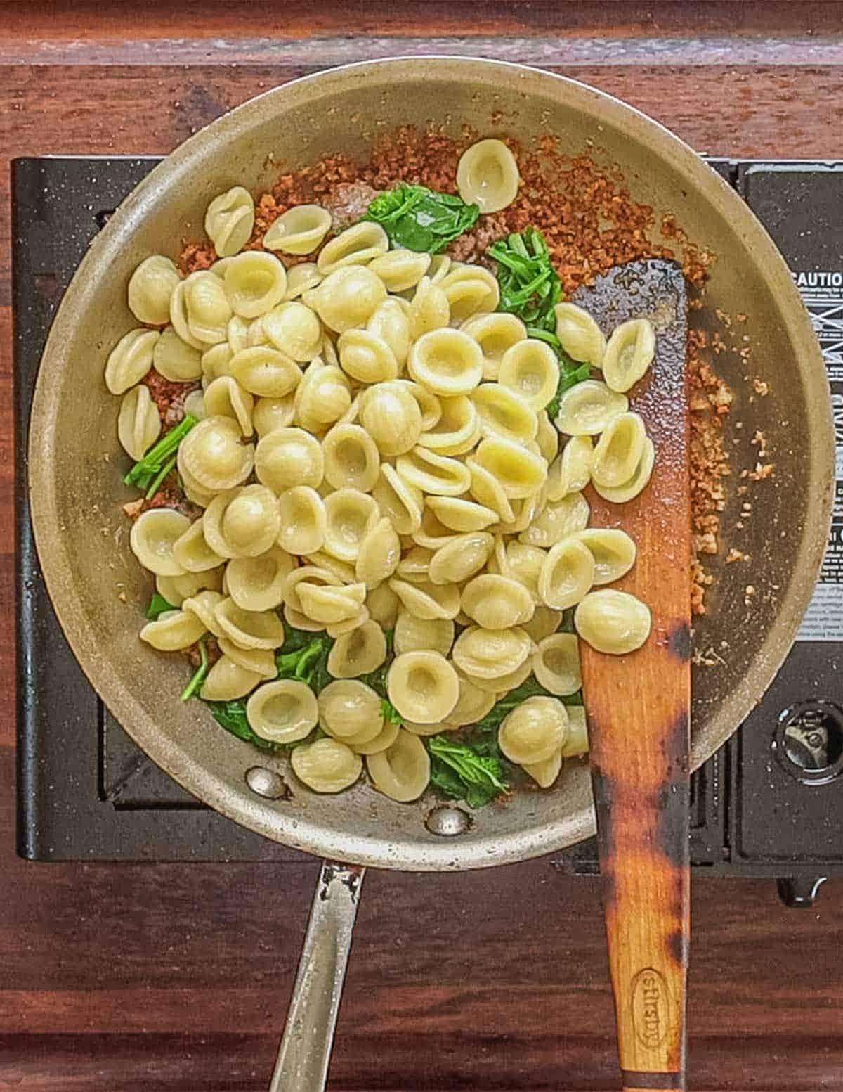 Tossing cooked orechiette pasta with sausage, breadcrumbs and cooked broccoli rabe.