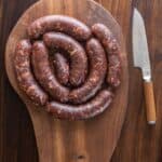 A coil of wild boar sausage on a cutting board next to a knife.
