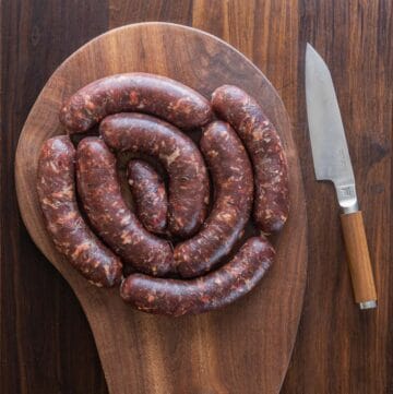 A coil of wild boar sausage on a cutting board next to a knife.