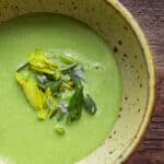 A bowl of asparagus end soup with herbs and vegetables in a ceramic bowl.