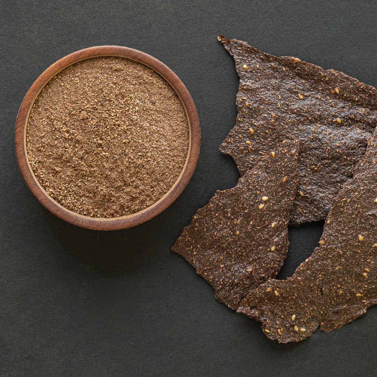 Dock seed flour crackers next to a bowl of ground dock flour on a black background. 