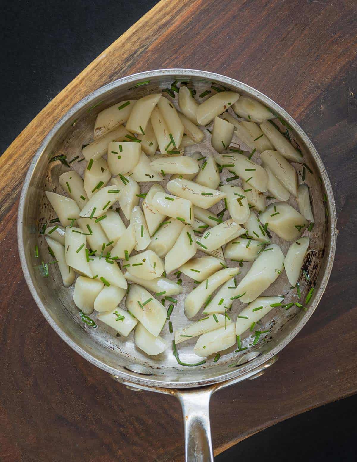 A top down image of a pan of thistle roots cooked with butter and chives. 