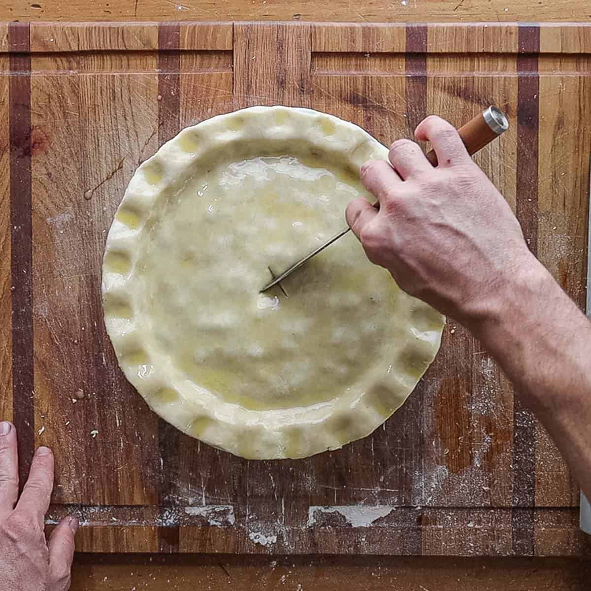 Cutting slits in the top of a pie crust before baking. 