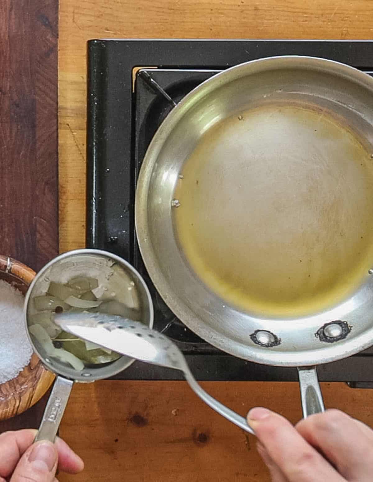 Removing cooked shallot, peppercorns and bay leaf from a sauce reduction. 