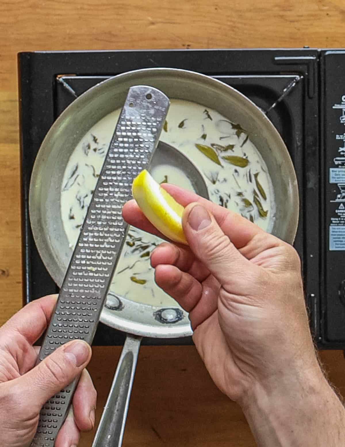 On overhead image showing lemon zest being grated into a sauce. 