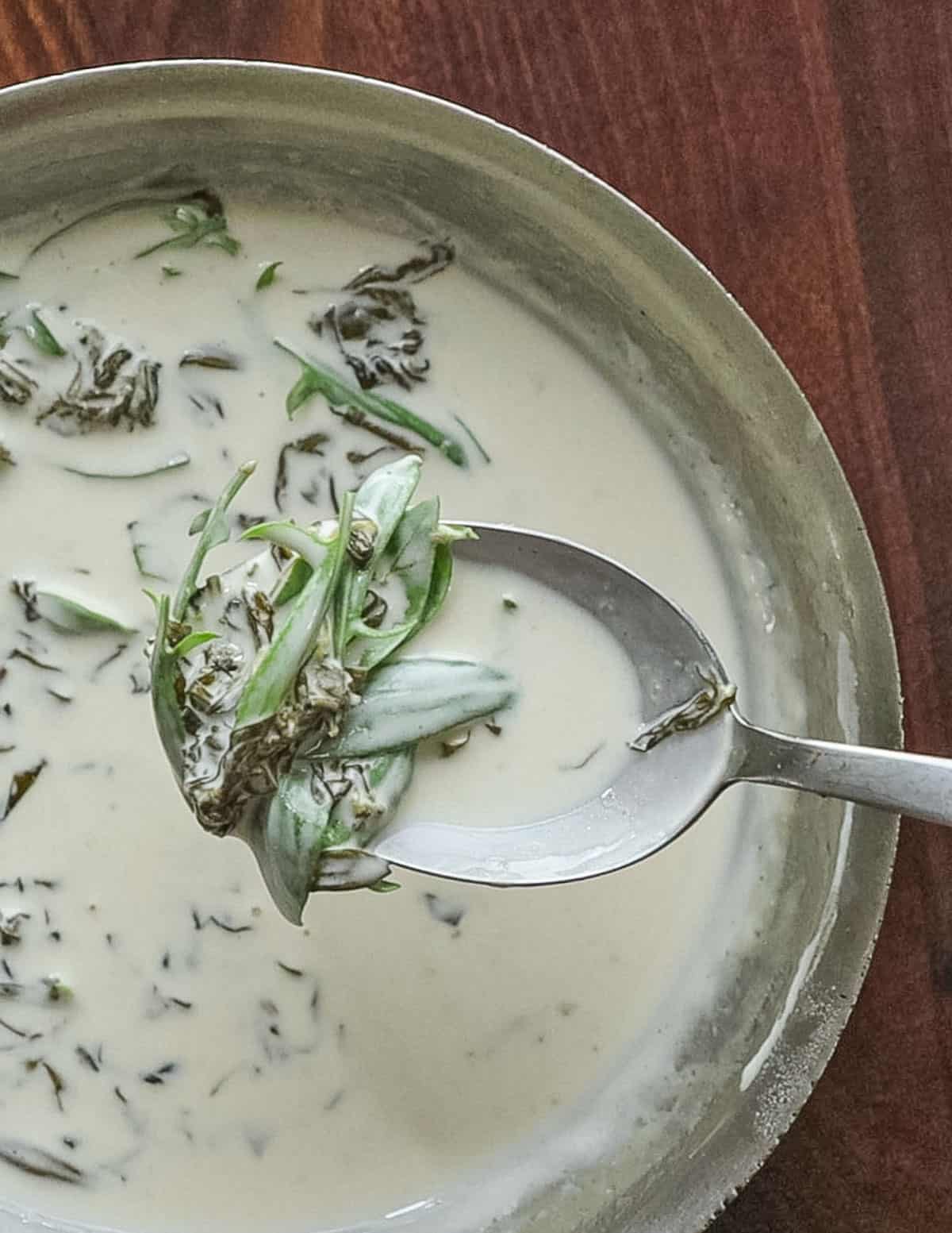 A finished pan of sheep sorrel sauce with a spoon filled with greens and sauce. 