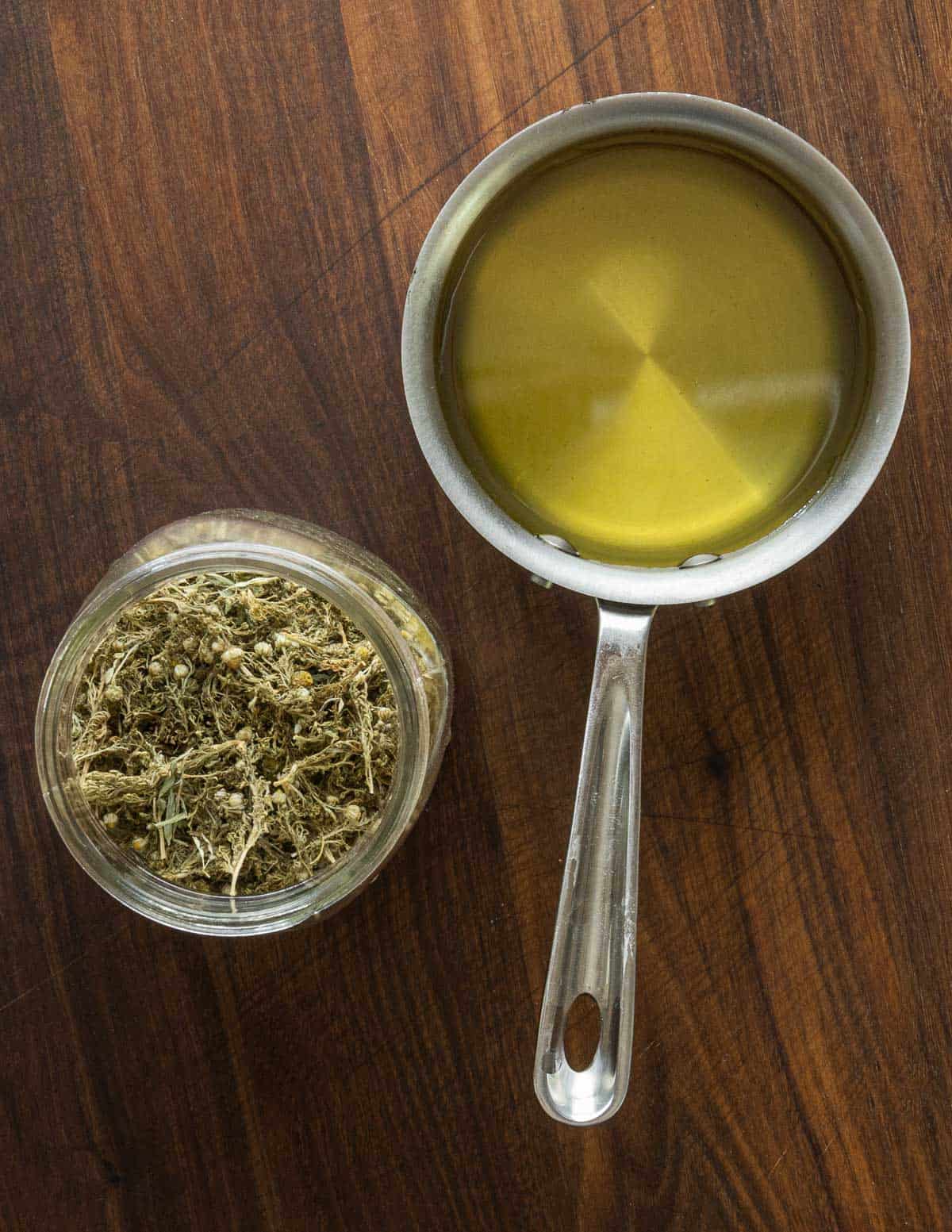 A small pan of yellow pineapple weed syrup next to a jar of dried pineapple weed flowers. 