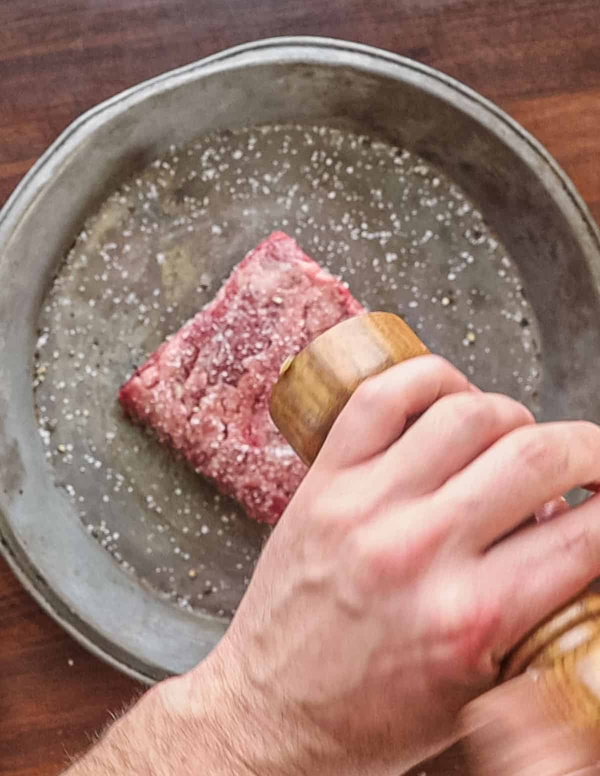 Seasoning a steak with pepper before cooking.