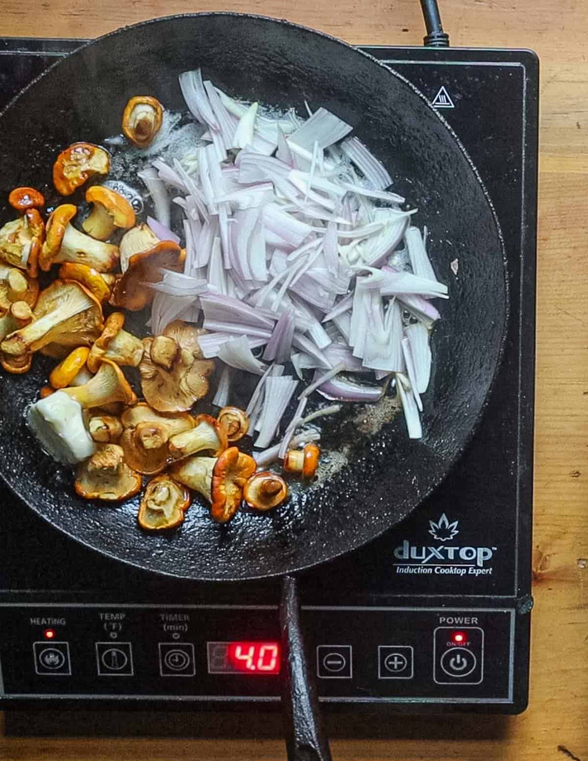 Adding shallots to a pan of cooked mushrooms. 