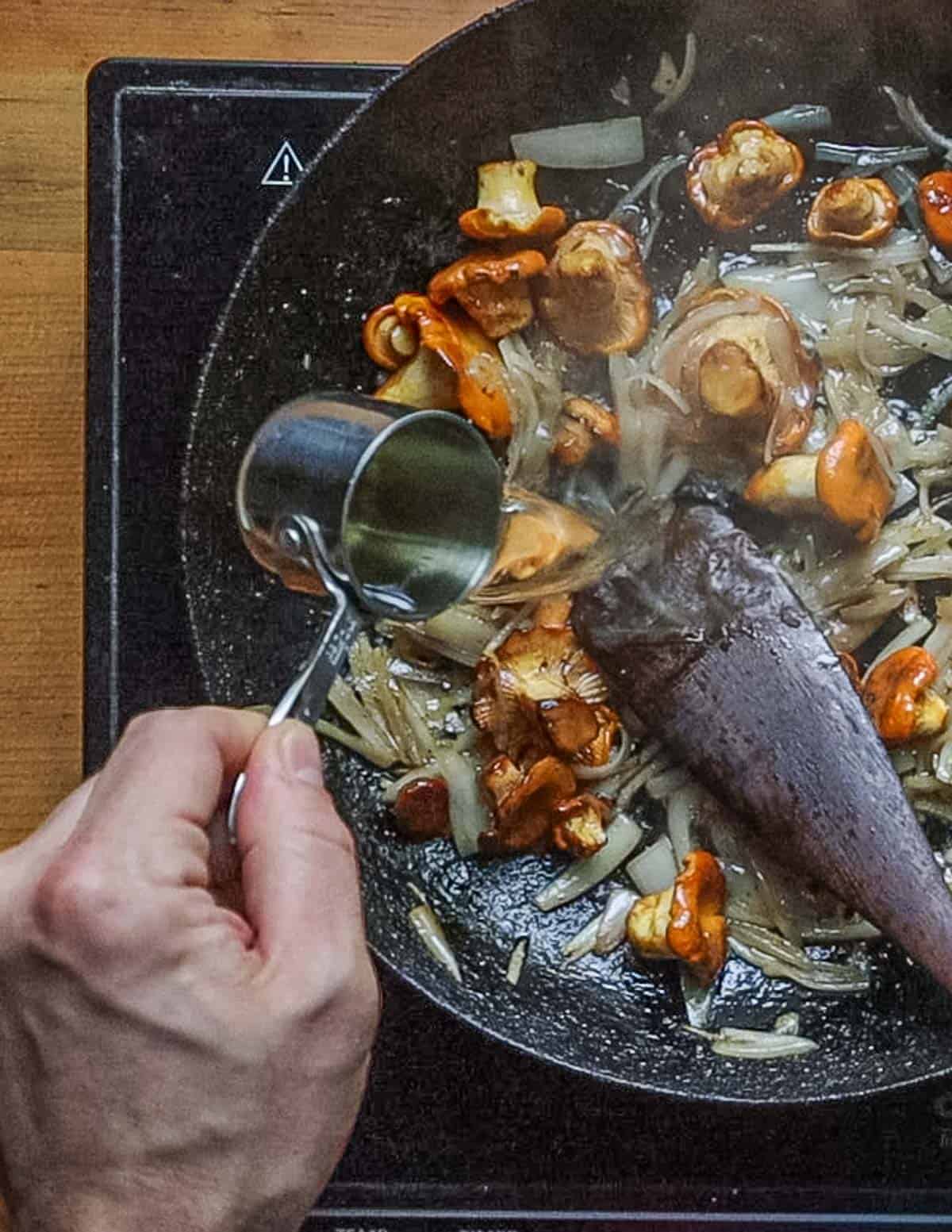 Adding wine to a pan of mushrooms and shallots. 