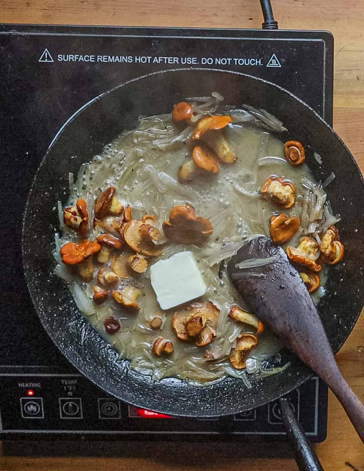 Adding butter to a pan of mushrooms, shallots and herbs. 