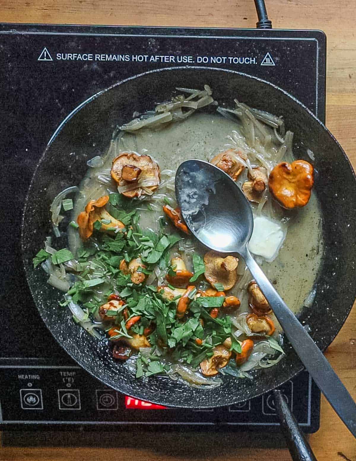 Adding butter to a pan of mushrooms, shallots and herbs. 