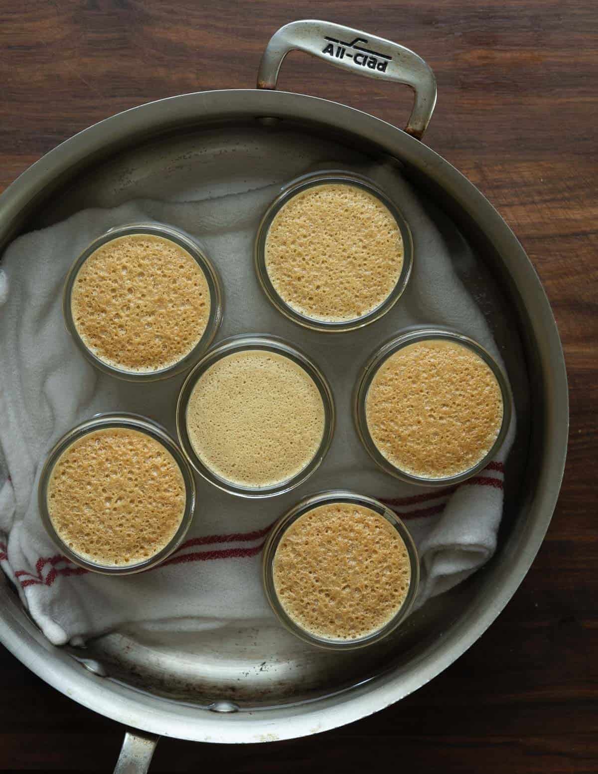 Top down image of a pan cooked linden custards in ramekins in a steel  pan. 