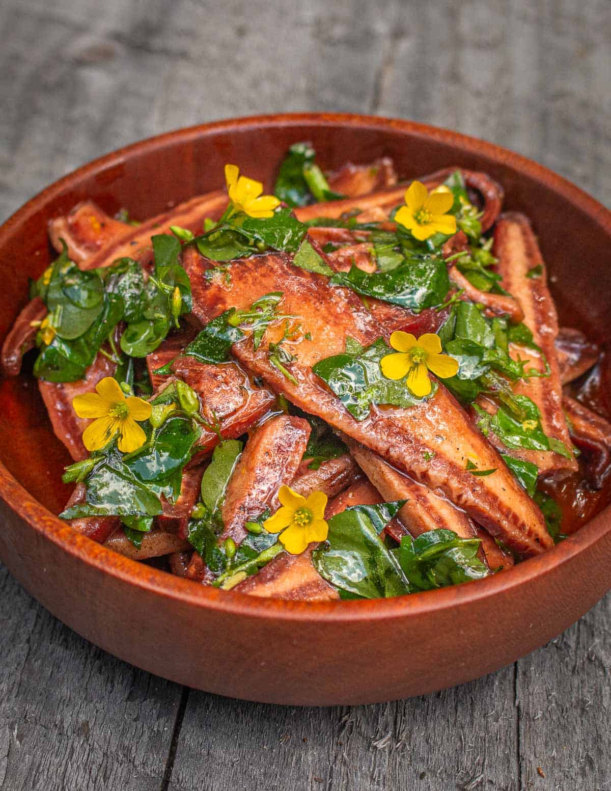 A wooden bowl filled with sliced mushrooms dressed with olive oil and sorrel flowers. 